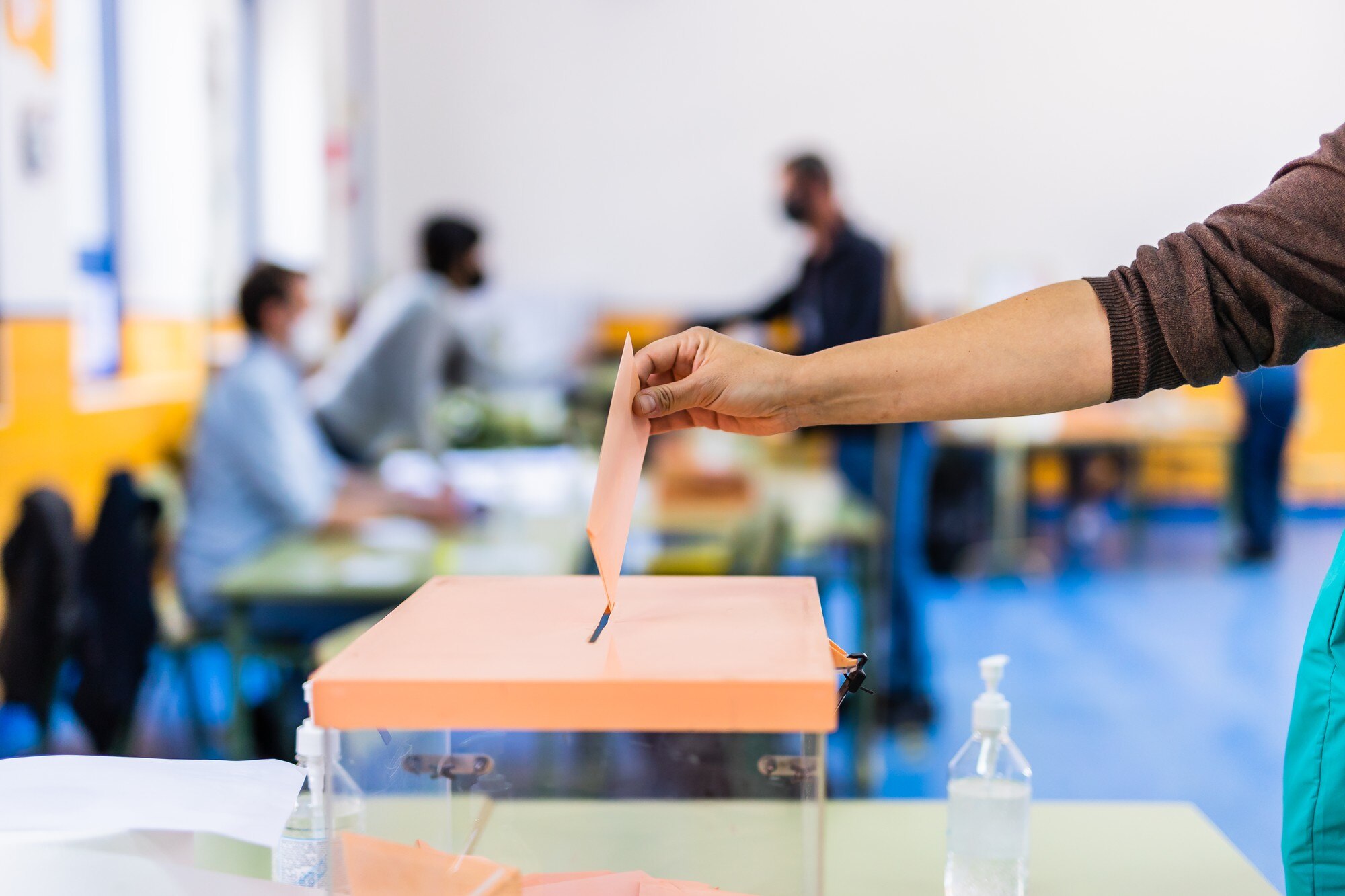 A voter inserts a ballot into a clear box with an orange lid at a polling station in Madrid.