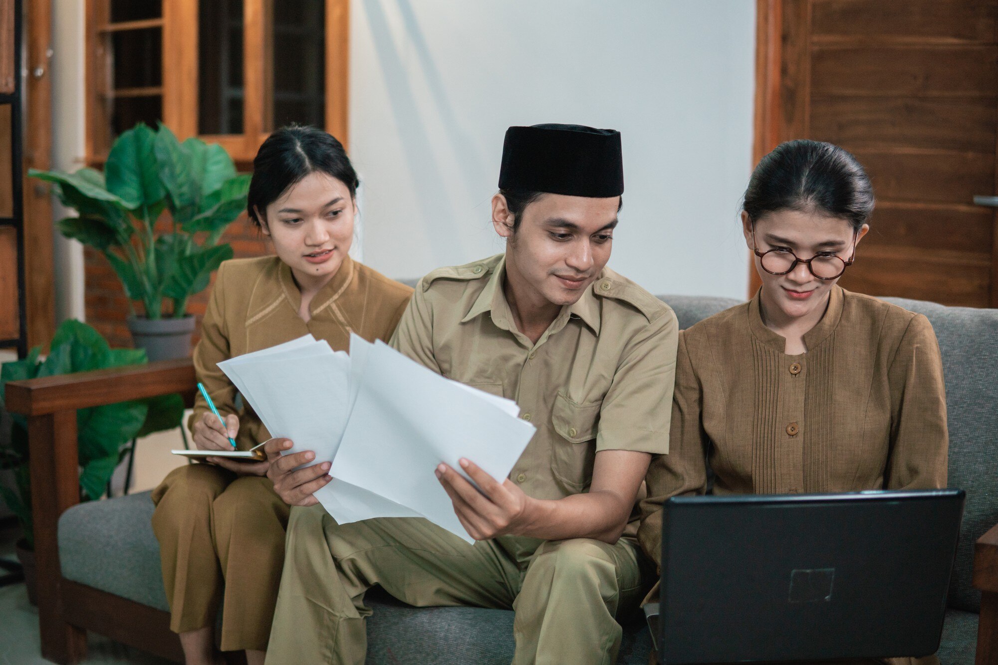 Three colleagues review papers and a laptop while seated together in an office.