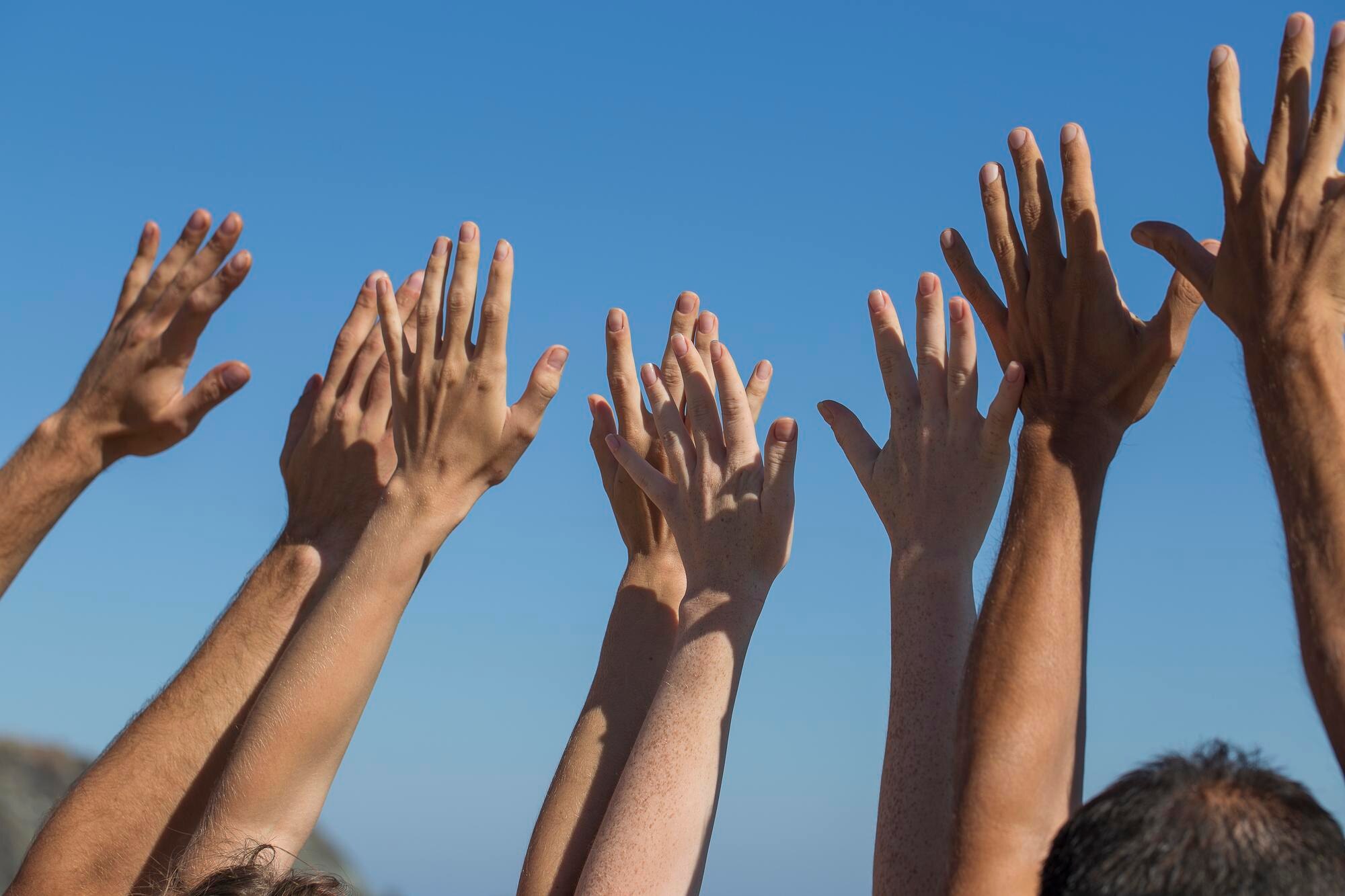 People raising their hands outdoors against a clear blue sky.