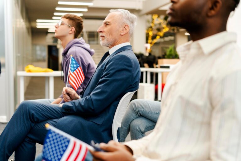 Seated attendees listen attentively, with two holding small American flags.